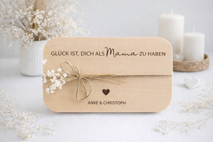 Hochwertiges Frühstücksbrett aus Holz mit eingravierter Botschaft „Glück ist, dich als Mama zu haben“, personalisiert mit zwei Namen und Herzsymbol, stilvoll inszeniert mit Kerzen und zarter Deko – emotionales Geschenk für Mama von Kindern.