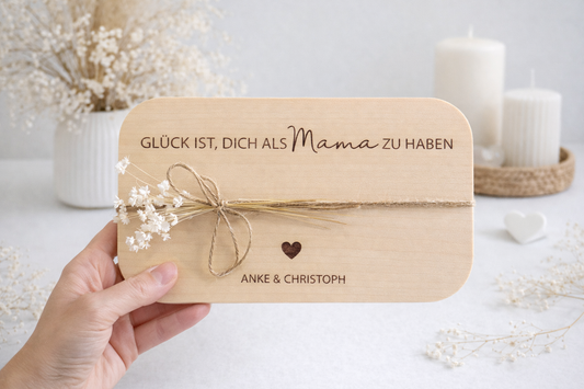 Personalisiertes Holzbrett aus hellem Holz mit Gravur „Glück ist, dich als Mama zu haben“ und Namen Anke & Christoph, dekoriert mit Juteband und weißen Trockenblumen auf modernem hellweißen Hintergrund – liebevolles Geschenk für Mama zum Muttertag, Geburtstag oder Weihnachten.