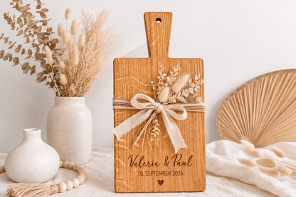 Personalisiertes Holzbrett zur Hochzeit mit Namen des Brautpaares und Hochzeitsdatum, dekoriert mit Trockenblumen und Schleife – individuelle Geschenkidee.
