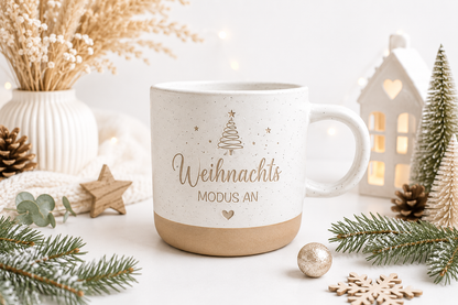 Keramiktasse mit weihnachtlichem Spruch „Weihnachtsmodus an“, dekoriert mit Tannenzweigen, Zapfen und Sternen. Eine liebevolle Aufmerksamkeit zum Wichteln, Nikolaus oder Advent