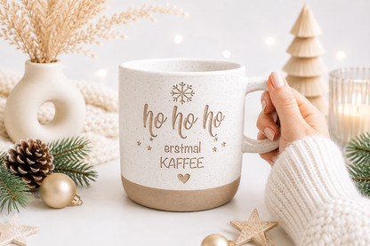 Weihnachtstasse aus Keramik mit Spruch „Ho Ho Ho erstmal Kaffee“, liebevoll in einer Hand gehalten, mit dezenter Weihnachtsdeko. Originelle Geschenkidee für Kaffeeliebhaber.
