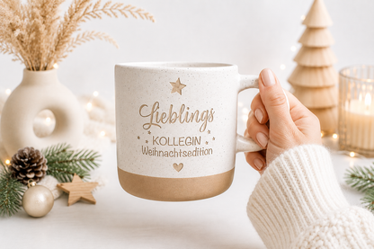 Personalisierbare Steingut Tasse mit weihnachtlichem Motiv und Gravur, dekoriert mit Tannenzweigen und Zapfen. Ideal als Wichtelgeschenk für die Kollegin oder als kleine Überraschung im Adven
