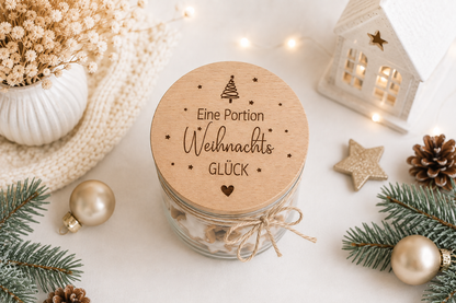 Dekoratives Vorratsglas mit graviertem Holzdeckel, Weihnachtsbaum, Sternen und Spruch „Eine Portion Weihnachtsglück“ in festlicher Weihnachtsdekoration.